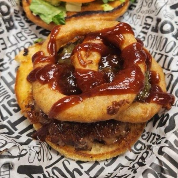 Mixed Up Burgers' burger with onion rings and barbecue sauce on branded paper.
