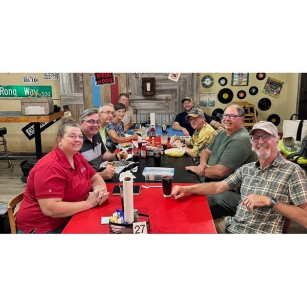 A group of people enjoying burgers and drinks at a long red table in Mixed Up Burgers.