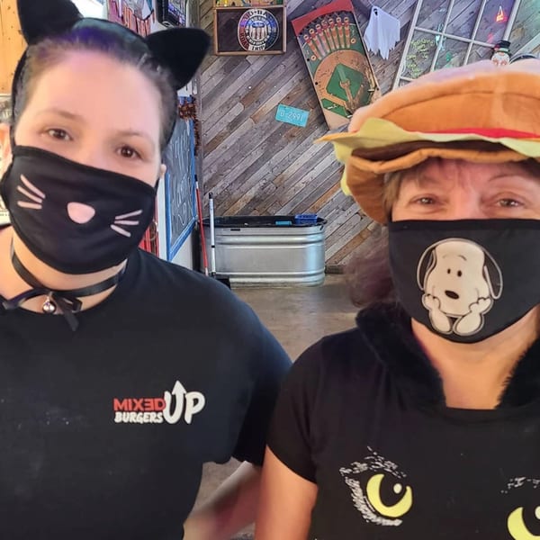 Two Mixed Up Burgers employees in festive masks and hats, one with cat ears and the other a burger.