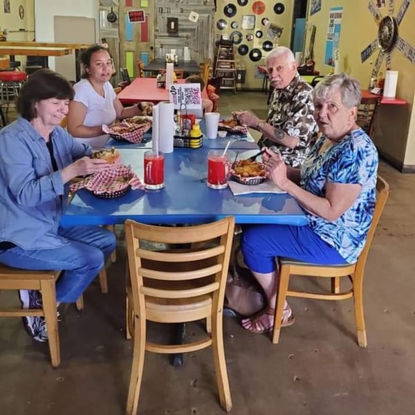 Four people eating burgers and fries at a blue table in Mixed Up Burgers restaurant.