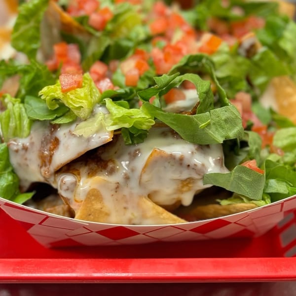 Mixed Up Burgers' nachos with white sauce, lettuce, and diced tomatoes in a red checkered tray.