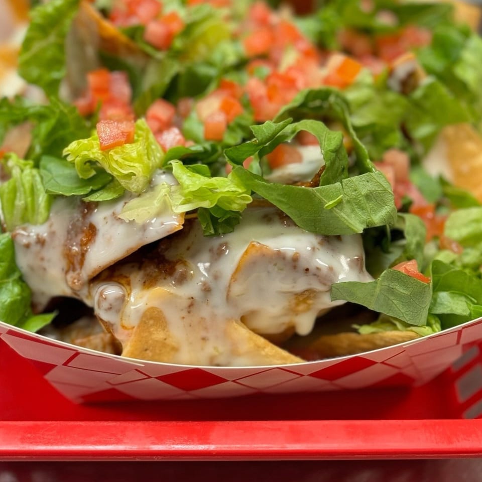 Mixed Up Burgers' nachos with white sauce, lettuce, and diced tomatoes in a red checkered tray.