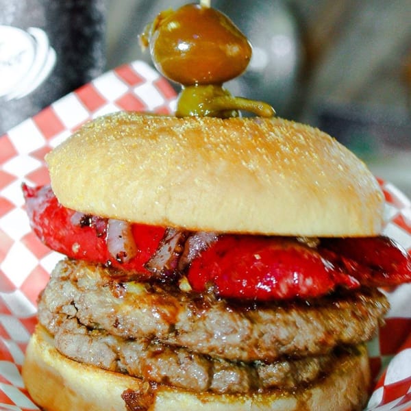 A Mixed Up Burgers double patty burger with red peppers, onions, and a pickled pepper on top.