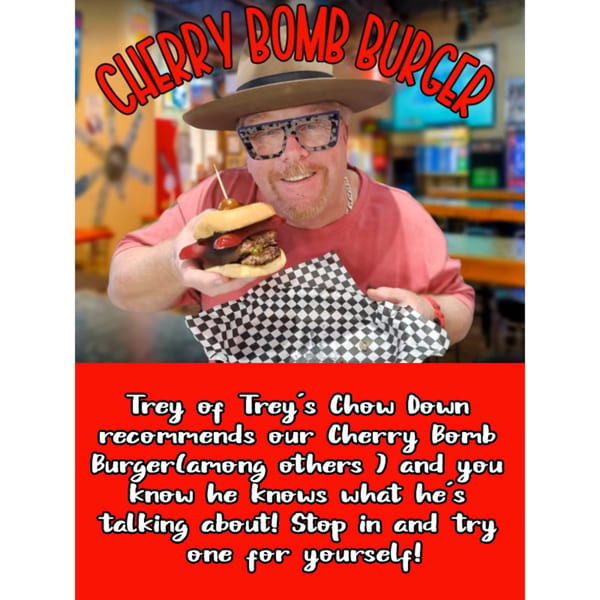 A man in a hat and glasses smiles while holding a Cherry Bomb Burger from Mixed Up Burgers.