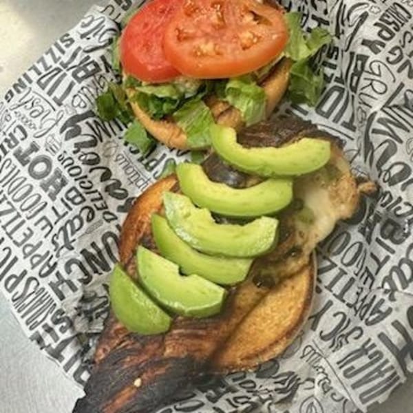 An open-faced Mixed Up Burger with avocado slices, lettuce, and tomato on branded paper.