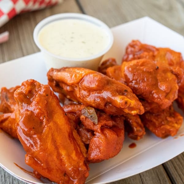 A white paper tray filled with buffalo chicken wings and a side of ranch dressing.